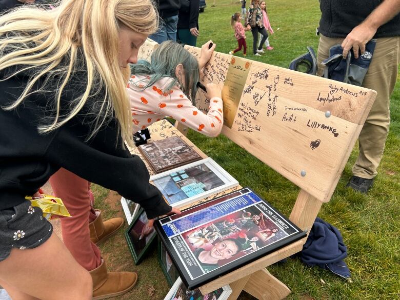 Two girls signing a wooden bench.