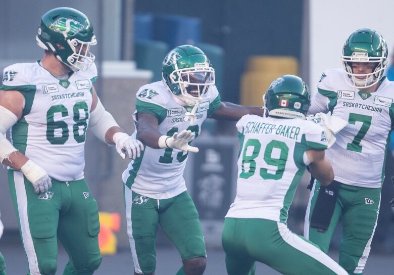 A group of football players in white-and-green uniforms are celebrating on the field.