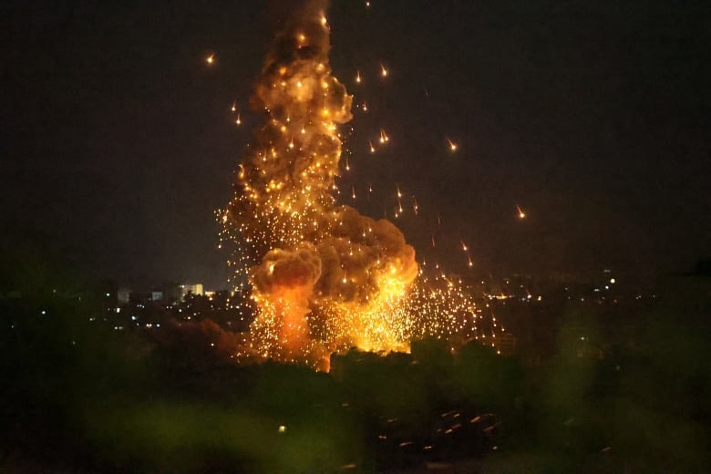 A large plume of fire, smoke and debris rise from above a city following a nighttime air strike.