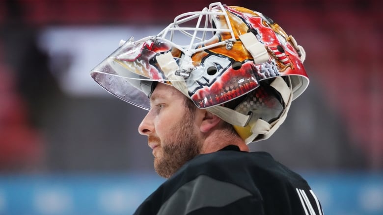 A hockey goaltender has his mask tilted up on his head during a break in a practice.