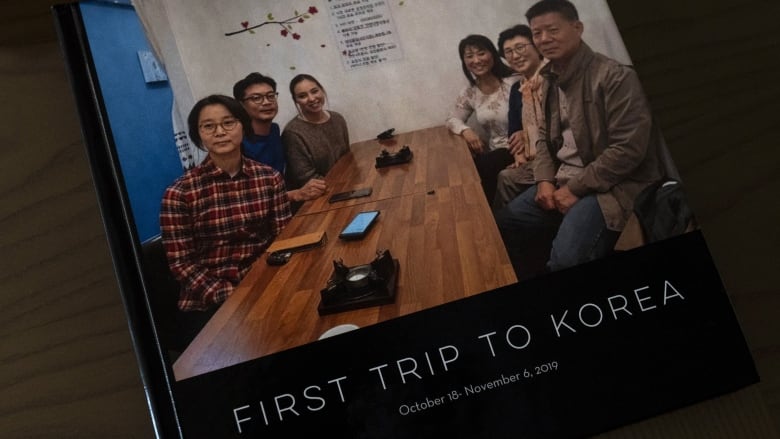 Six people are shown at a dinner table, three on each side in a photograph that appears on the cover of a book that reads, 'First Trip to Korea.' 