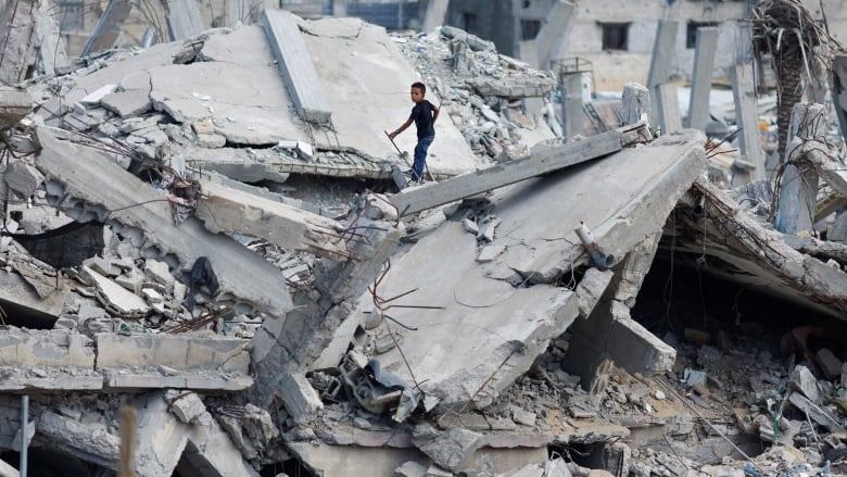 A boy stands on the rubble of a destroyed house.