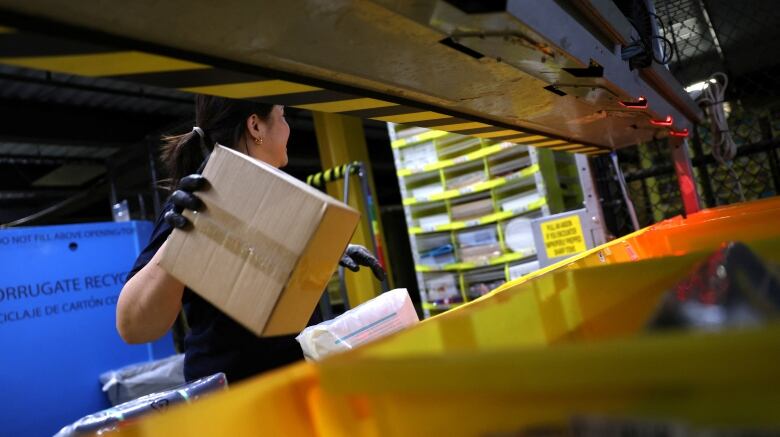 Seemingly taken from within a yellow bin on the production line, this image shows a worker on a production line, turned away from the camera, holding a box in one hand. 