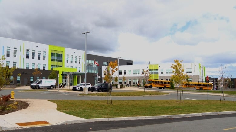 A white, grey and lime green high school. There are cars and yellow school buses parked in front of the building. 