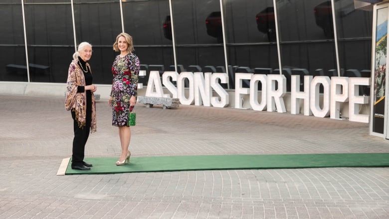 Two women standing next to a green carpet.