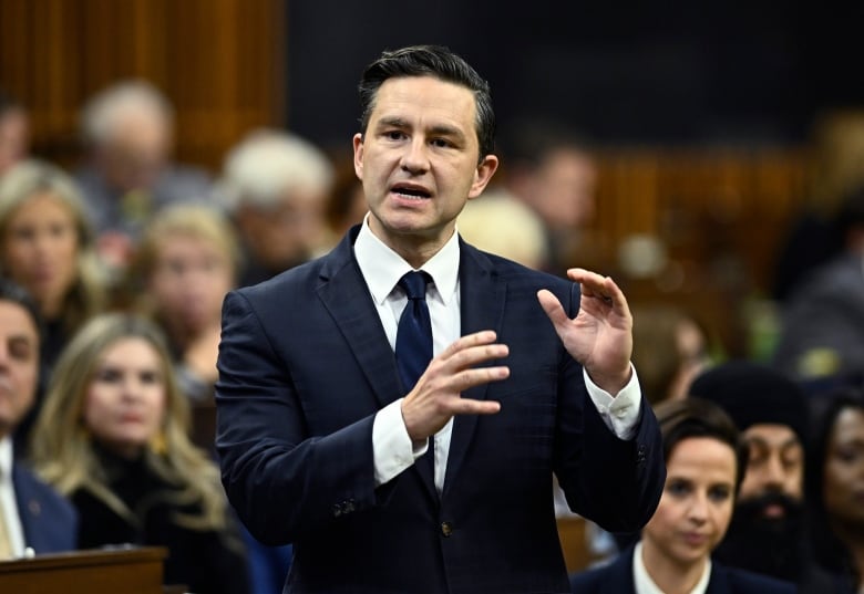 A man in a dark suit gestures with his hands as he speaks in the House of Commons.