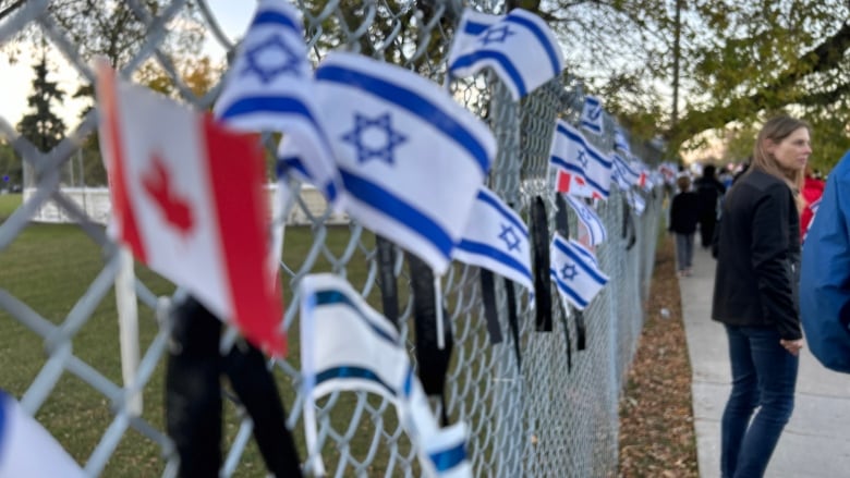 Small Israeli and Canadian flags are seen placed in fencing as people walk by.