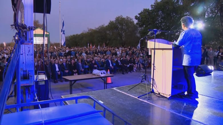 A person is seen speaking at a podium to a crowd of people.