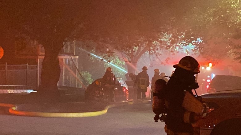 Firefighters standing in front of a burning home at night. 