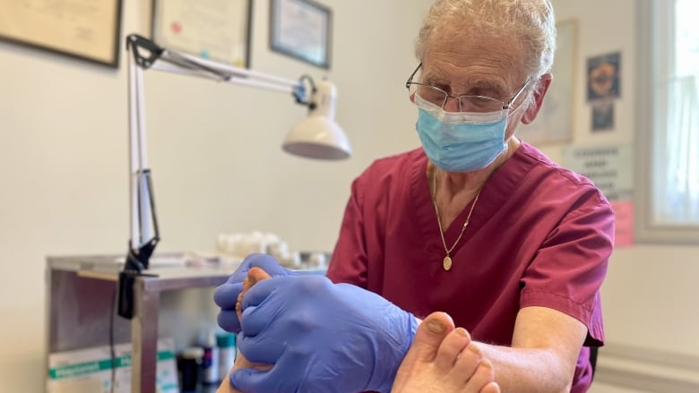 Podiatrist Keith Bettles wears medical gloves and a mask and works on two feet in front of him. 