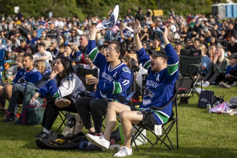 Groups of hockey fans, in a park, seem to celebrate something offscreen.