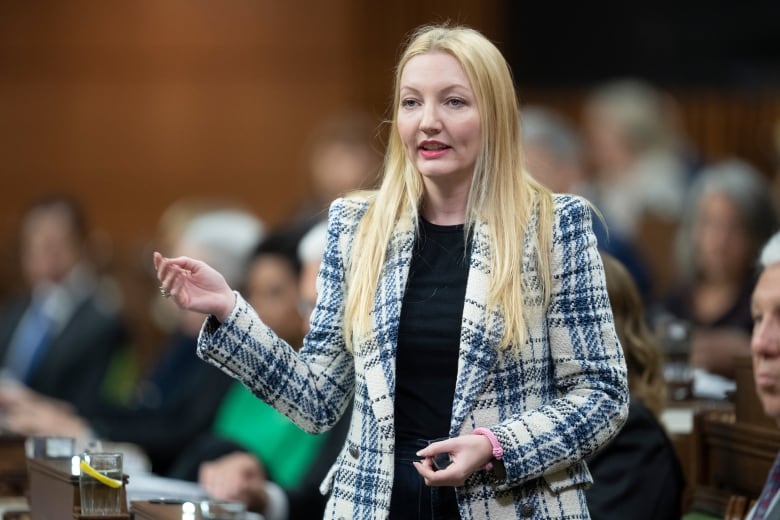 A woman wearing a white and blue coat speaks in the House of Commons.