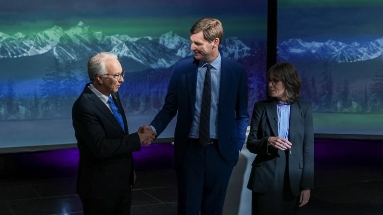 Two men shake hands as a woman looks on.