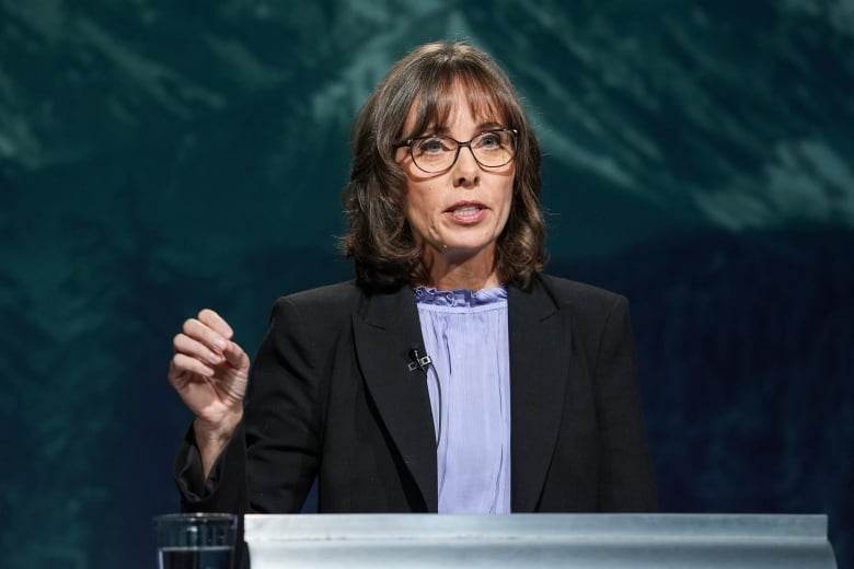 A woman raises her hand as she speaks at a podium.