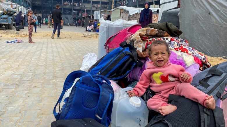 A child crying sits on top of bags at a refugee camp.