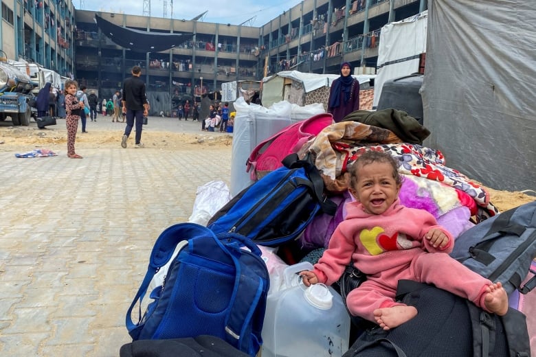 A child crying sits on top of bags at a refugee camp.