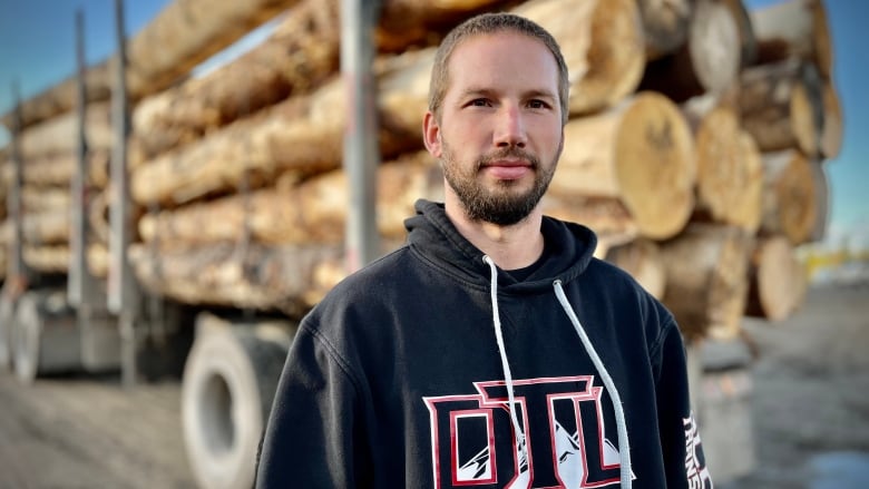 A man with a beard in front of a logging truck. 