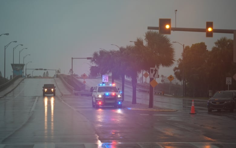 Two vehicles are shown on a roadway with their lights on, in a semi-darkened sky.