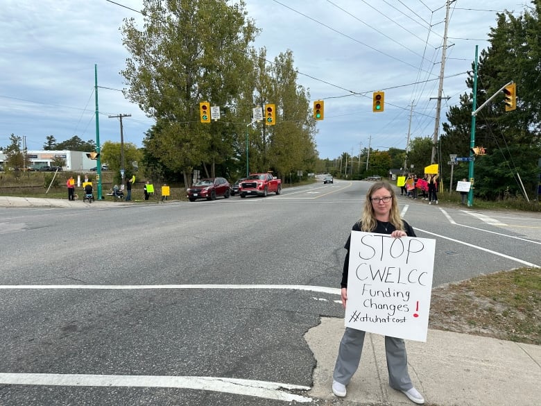 Anya Kerr standing in next to an intersection holding a sign that says 