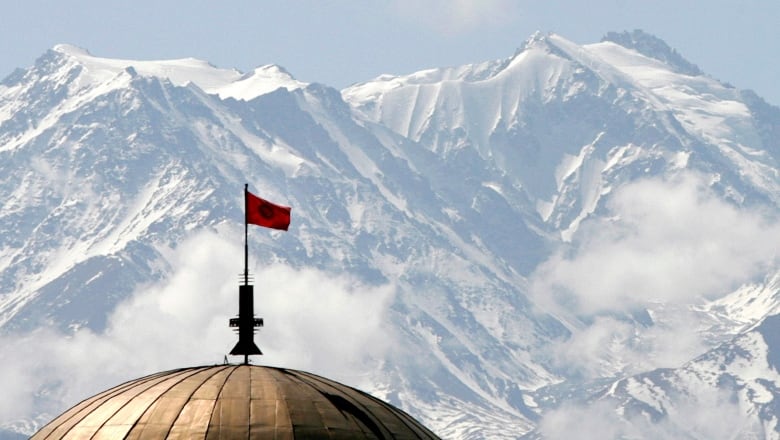 Tian-Shan mountains rise above the Kyrgyzstan's capital Bishkek, with a Kyrgyz flag atop a building in the foreground.