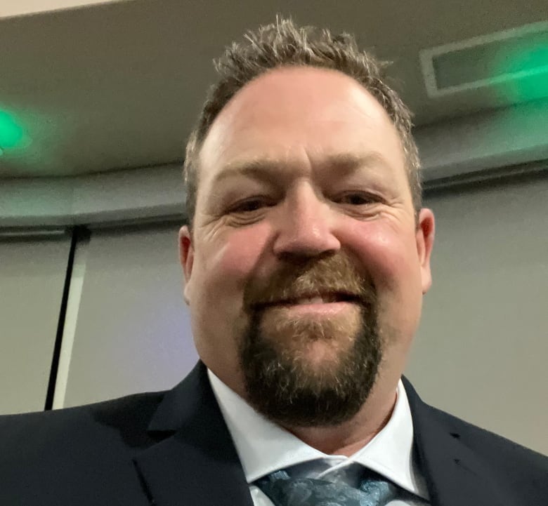 A headshot of a smiling man with a dark brown goatee and who's wearing a suit. 