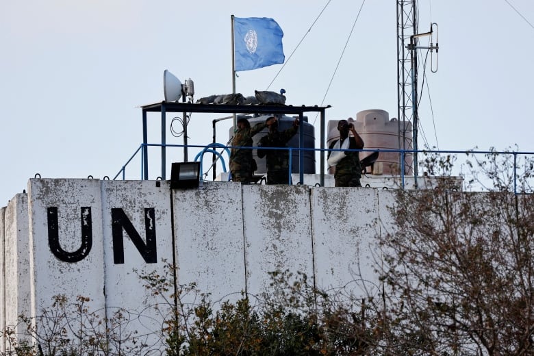 Men in military uniforms stand on a watch tower with a UN flag and the letters 