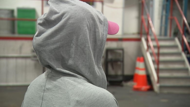 A person in a grey hoody, from behind with the hood up, looks off screen.