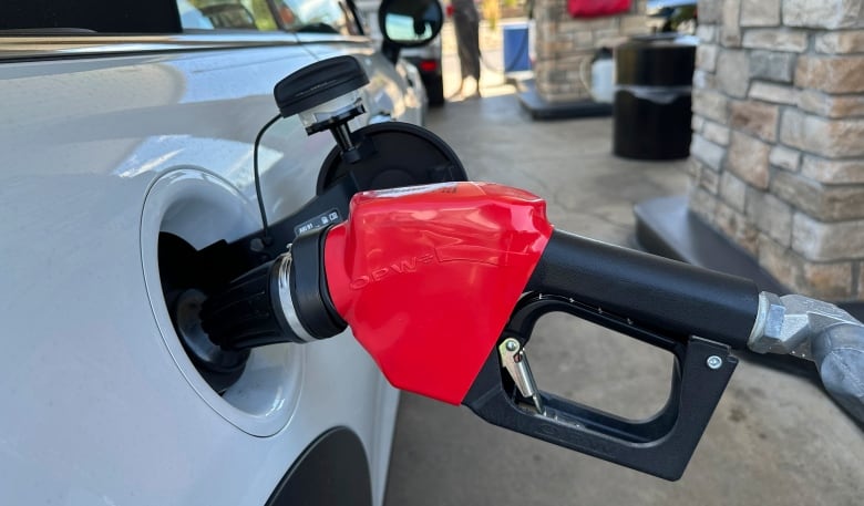 A close-up of a gas nozzle plugged in the gas opening of a white car. 