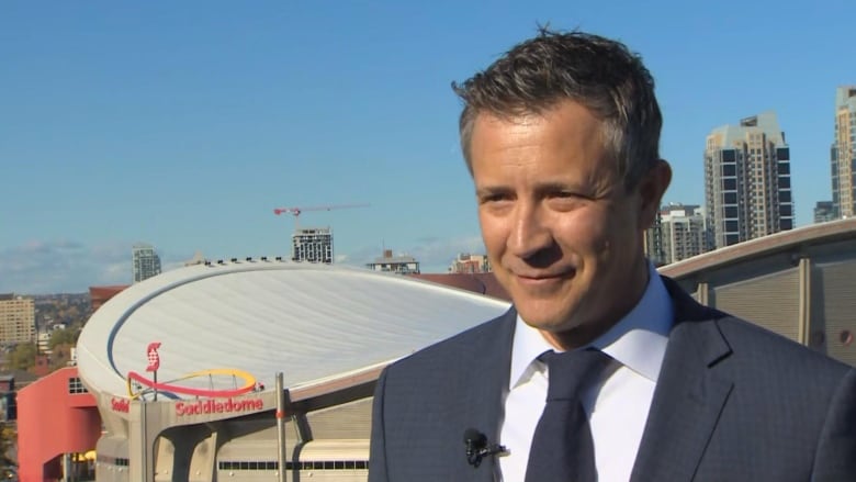 A man wearing a suit and tie stands in front of a sports stadium.