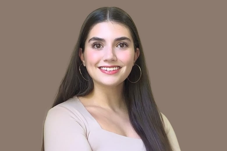 A girl with long brown hair poses for a headshot. She wears a pale pink shirt and silver hoop earrings. 