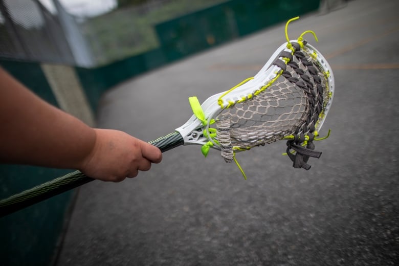 Hand holds green lacrosse stick.