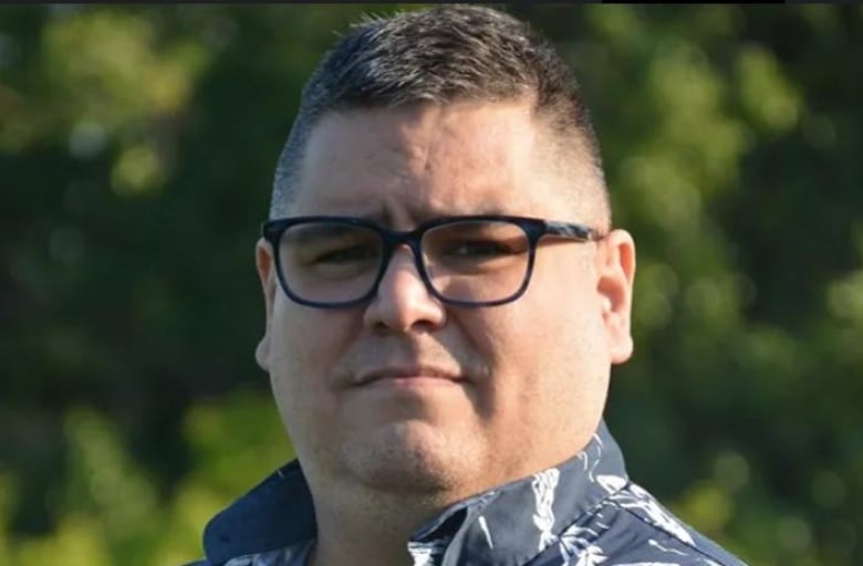 A man with glasses and short hair in a collared shirt poses for a picture outdoors.