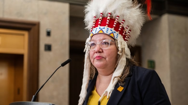 A woman in a headdress speaks at a podium.