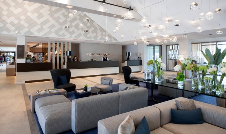 Wide view of a high end hotel lobby with grey couches and green and white flower pots.