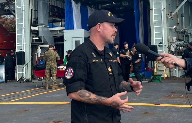 A master sailor in navy uniform speaks with a reporter on the deck of a patrol ship