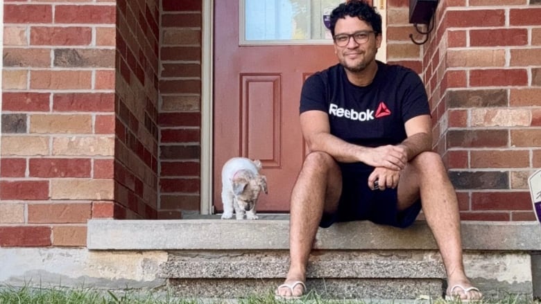 A man sits on a front porch of a house with a puppy.