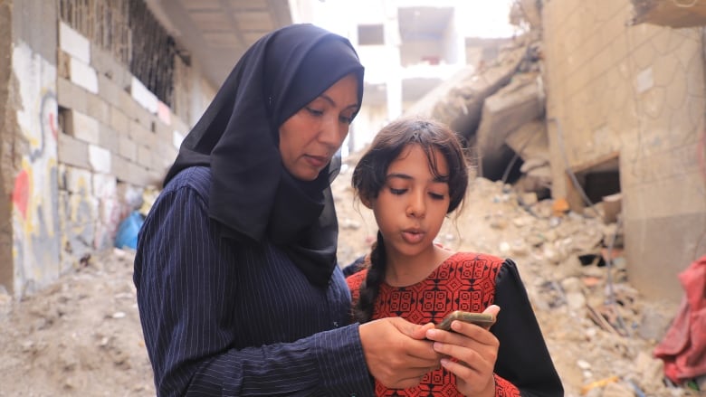 A woman and her daughter look at a text on a cellphone.