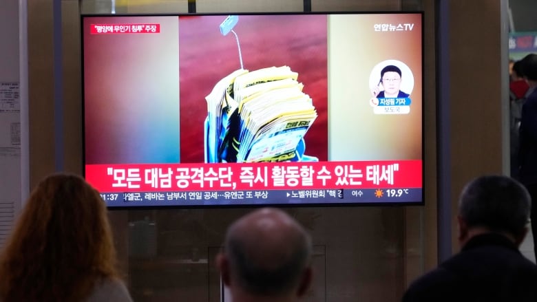 The backs of three people are shown as they face toward a television screen that has Asian script displayed alongside images.