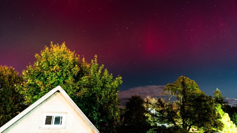 The top of a house with night sky behind and the northern lights visible.