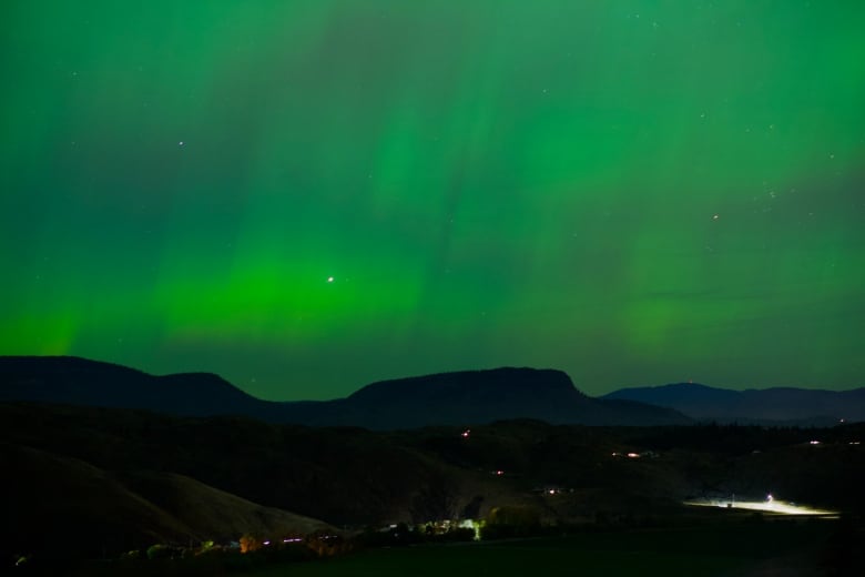 Green lights dominate the sky above the silhouette of mountains