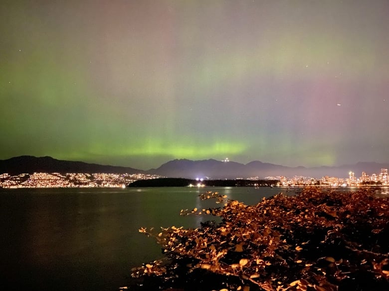 A band of green in the sky above the silhouette of mountains. 