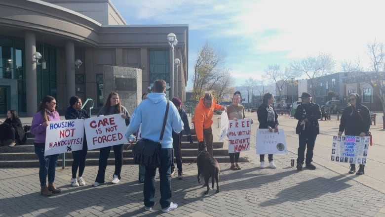 A group of people holding signs with slogans like 'Housing not handcuffs' and 'Care is not forced.'