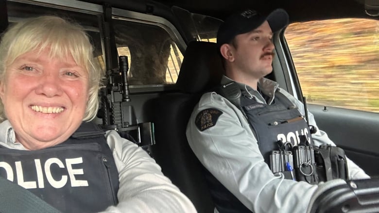 A female police officer takes a picture in a car, with a male officer driving. 