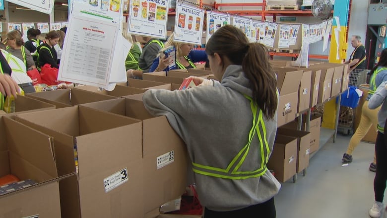 A person puts food into boxes, with other volunteers visible in the background. 