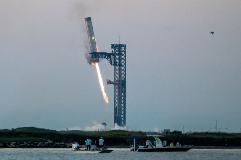 A booster rocket is grabbed by metal arms at the launch pad. 