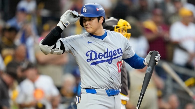 A male baseball player wearing a batting helmet tips the beak with his right hand while holding a bat in his left hand during a game.