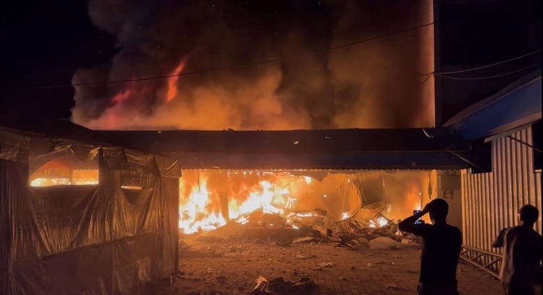 Two people watch a fire from a distance.