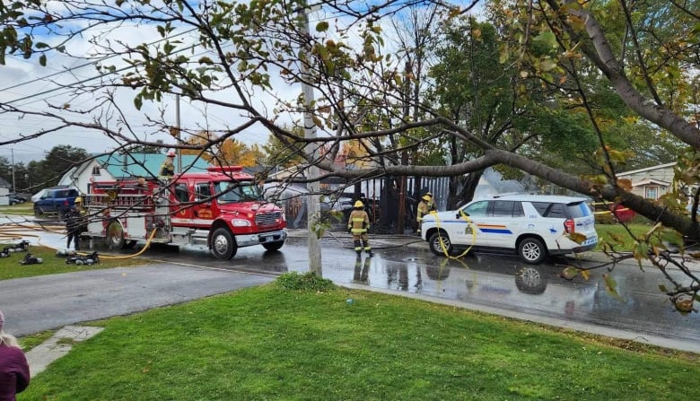 A street view with a firefighter truck and police vehicle. There is a smoking wooden structure that's mostly destroyed.