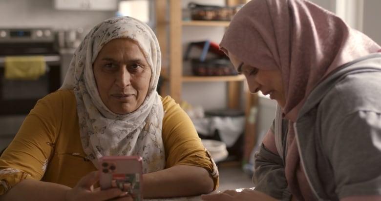 Two women sit at a table. One holds a cell phone.