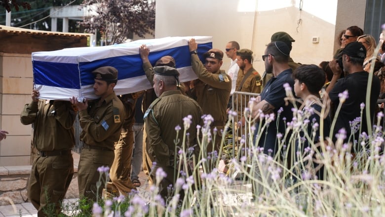 A coffin, draped in an Israeli flag, is carried by six men in military uniforms.